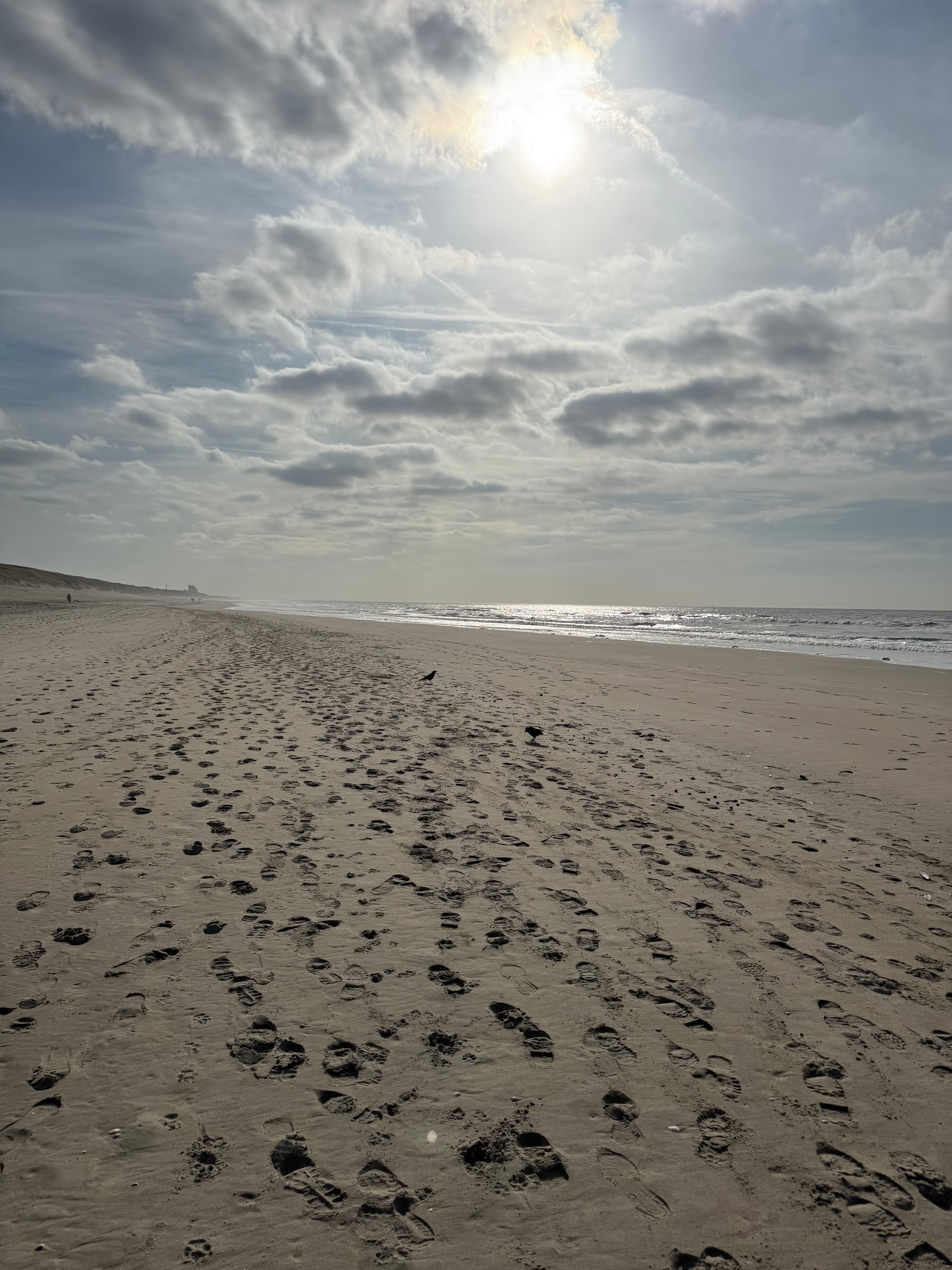 Voetstappen over het brede strand van Noordwijk onder een wolkenlucht
